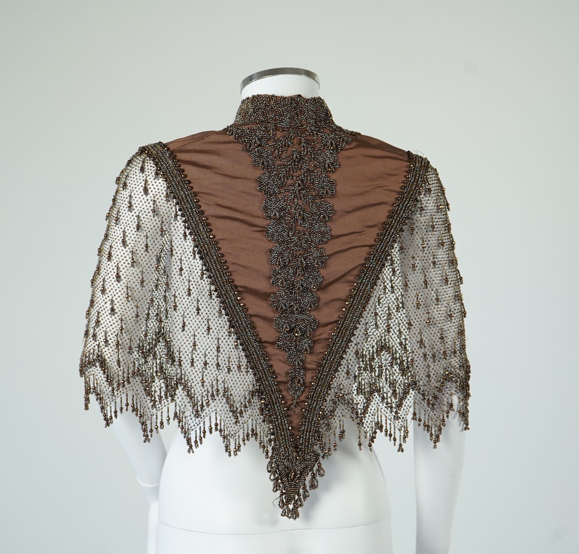 A late 19th century ladies ornate steel and brown beaded and fringed shoulder cape. Made as three ribbed silk panels with ornate beaded appliqués with a beaded and fringed net sleeved cape. Top of neck to bottom of beadi